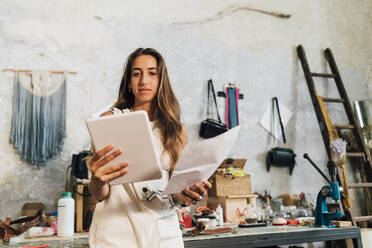 Modedesigner hält Papier und schaut auf einen Tablet-PC - MEUF07306