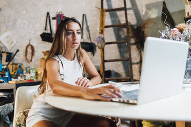 Modedesigner mit Laptop am Schreibtisch in der Werkstatt - MEUF07314