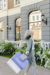 Frau genießt mit Einkaufstüten vor einem Gebäude - SEAF01089