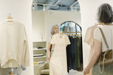 Frau beim Anprobieren eines Kleides vor einem Spiegel in einem Geschäft - SEAF01099