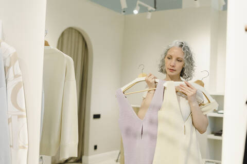 Woman looking in mirror trying on dresses at store stock photo