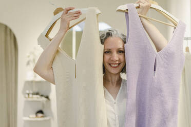 Happy woman holding dresses at store - SEAF01107