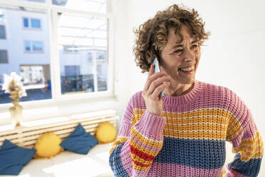 Happy woman with curly hair talking on smart phone at home - JOSEF11621