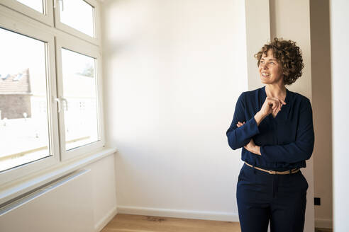 Smiling saleswoman looking through window in apartment - JOSEF11711