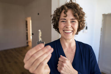 Happy saleswoman with curly hair showing house key - JOSEF11721