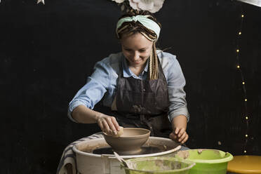 Smiling potter moulding shape on pottery wheel at art studio - LLUF00798