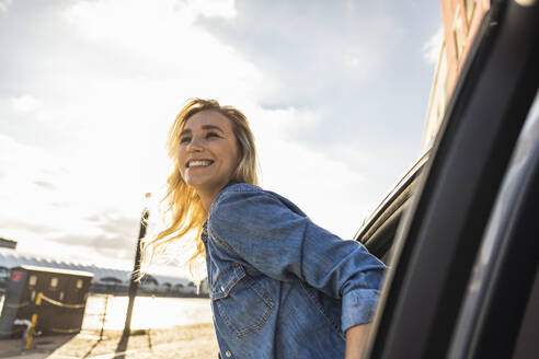 Smiling young woman leaning out of car window at sunset - UUF27003