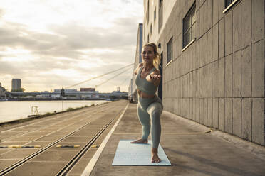 Glückliche blonde Frau übt Yoga auf der Promenade - UUF27017