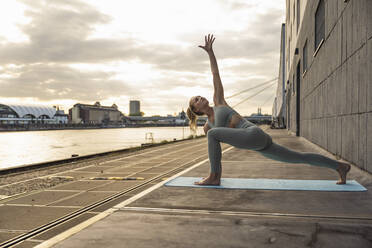 Junge Frau mit erhobener Hand übt Yoga auf der Promenade - UUF27018