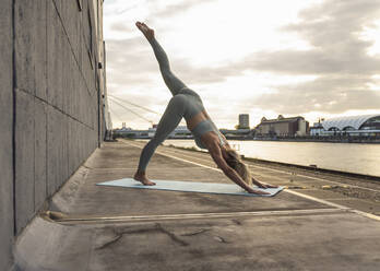 Woman practicing stretching exercise on promenade at sunset - UUF27022