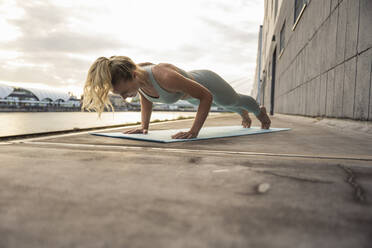 Blond woman practicing exercise on mat at promenade - UUF27026