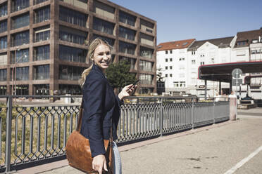 Happy blond woman with smart phone walking on road - UUF27043