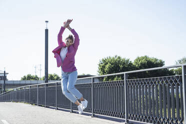 Happy young woman jumping in front of railing - UUF27050