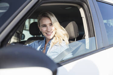 Happy blond woman sitting in car on sunny day - UUF27051