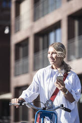 Glückliche Frau mit Fahrrad und Smartphone an einem sonnigen Tag - UUF27053
