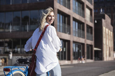 Lächelnde junge Frau mit Fahrrad an einem sonnigen Tag - UUF27055
