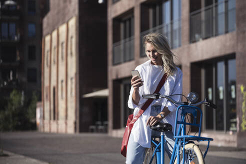 Glückliche junge Frau, die ein Mobiltelefon auf dem Fahrrad benutzt - UUF27058