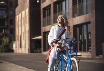 Lächelnde Frau genießt das Sonnenlicht auf dem Fahrrad sitzend - UUF27059