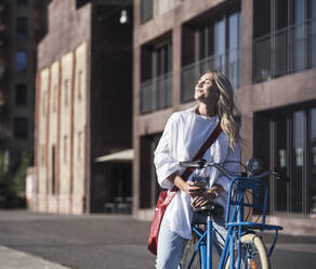 Happy young woman enjoying sunlight sitting on bicycle - UUF27060