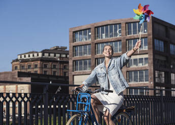 Glückliche Frau mit Windrädern auf dem Fahrrad an einem sonnigen Tag - UUF27066