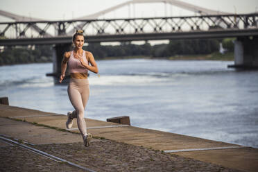 Smiling young woman jogging by river at promenade - UUF27069