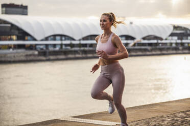 Happy woman jogging on promenade at sunset - UUF27071