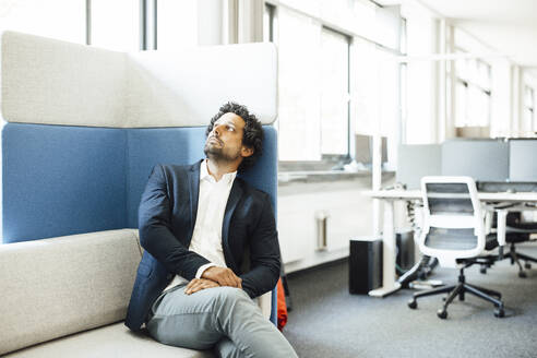 Thoughtful businessman sitting on sofa at workplace - JOSEF11756