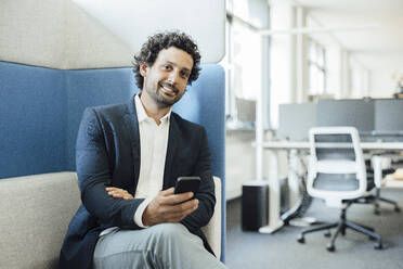 Lächelnder Geschäftsmann mit Smartphone im Büro - JOSEF11757