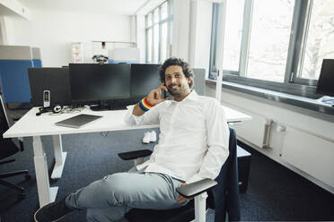 Smiling businessman talking on smart phone sitting in office - JOSEF11762