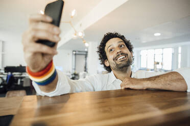 Lächelnder Geschäftsmann nimmt Selfie auf Handy im Büro - JOSEF11768