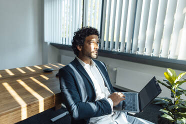 Thoughtful businessman with laptop in office - JOSEF11775