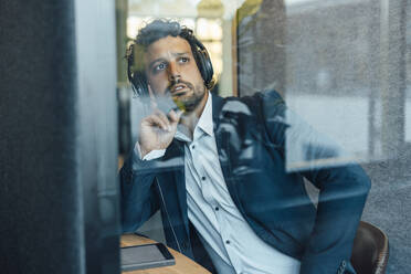 Nachdenklicher Geschäftsmann mit Headset durch das Glas eines Büros gesehen - JOSEF11781