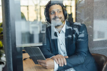 Lächelnder Geschäftsmann mit Headset und Tablet-PC durch Glas im Büro gesehen - JOSEF11783