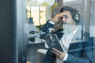 Businessman using tablet computer seen through glass of workplace - JOSEF11784