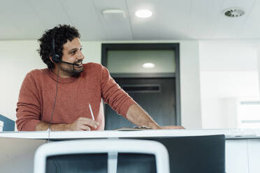 Businessman talking over headset at workplace - JOSEF11810