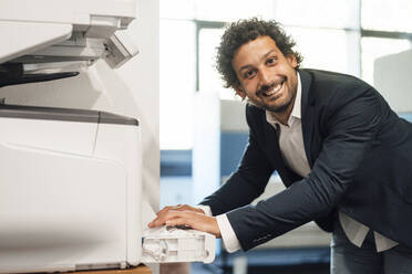 Smiling businessman using computer printer at office - JOSEF11822