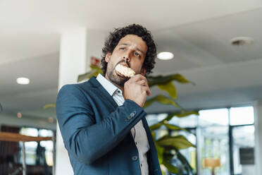 Businessman eating flavored ice cream in office - JOSEF11840