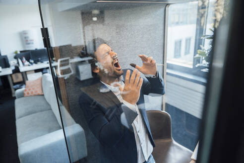 Angry businessman shouting in soundproof cabin at office - JOSEF11848