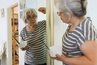 Ältere Frau, die weißes Haar untersucht und sich zu Hause im Spiegel betrachtet - MRRF02245