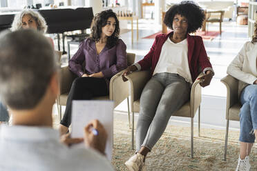 Nachdenkliche afroamerikanische Geschäftsfrau, die in einer Brainstorming-Sitzung im Büro Ideen mit Kollegen austauscht - JCICF00321