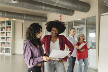 Businesswoman discussing over document with colleague in office - JCICF00344