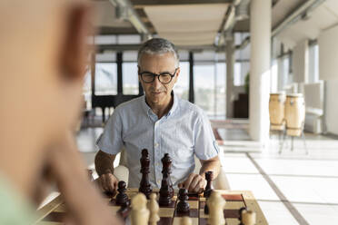 Älterer Geschäftsmann spielt Schach mit einem Kollegen im Büro - JCICF00358