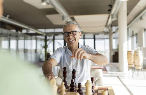 Glücklicher reifer Geschäftsmann spielt Schach mit einem Kollegen im Büro - JCICF00359