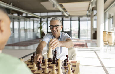 Lächelnder Geschäftsmann mit Brille spielt Schach mit einem Kollegen im Büro - JCICF00361