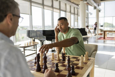 Businessman picking up chess piece playing board game with colleague in office - JCICF00363