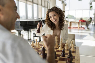 Glückliche junge Geschäftsfrau spielt Schach mit reifem Kollegen im Büro - JCICF00379
