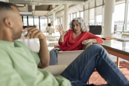 Ältere Geschäftsfrau bespricht Ideen mit einem Kollegen, der im Büro sitzt - JCICF00383