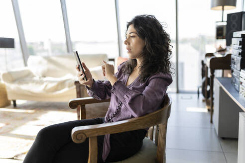 Geschäftsfrau mit Smartphone auf einem Stuhl im Büro sitzend - JCICF00385