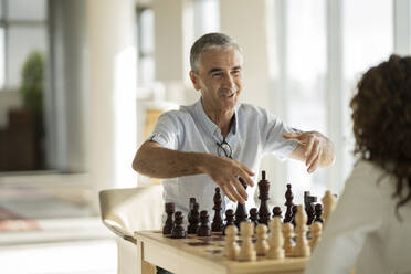 Lächelnder Geschäftsmann im Gespräch mit einem Schach spielenden Kollegen im Büro - JCICF00388