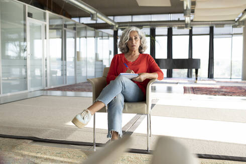 Ältere Geschäftsfrau mit gekreuzten Beinen auf einem Stuhl im Büro - JCICF00408